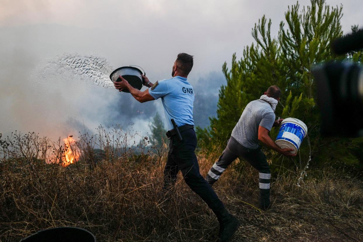 A police officer and a local resident throw buckets of water during a wildfire in Cascais (REUTERS)