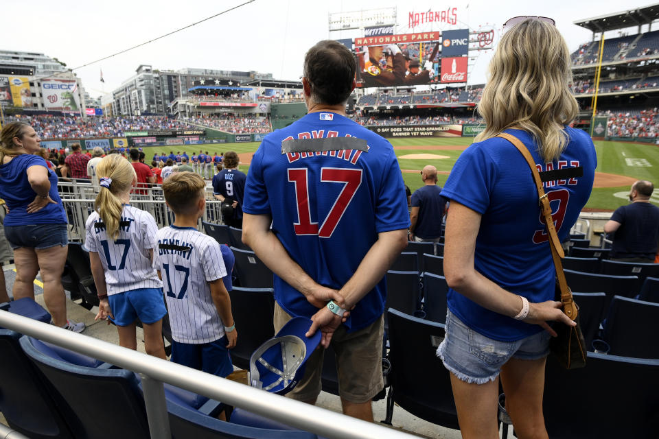 Chicago Cubs fans, from right to left, Kristin Chilcott, husband Mark, son Dexter and daughter Gemma, of Virginia, stand for the national anthem before a baseball game against the Washington Nationals, Saturday, July 31, 2021, in Washington. The family was wearing Cubs jerseys with traded players names taped over. (AP Photo/Nick Wass)