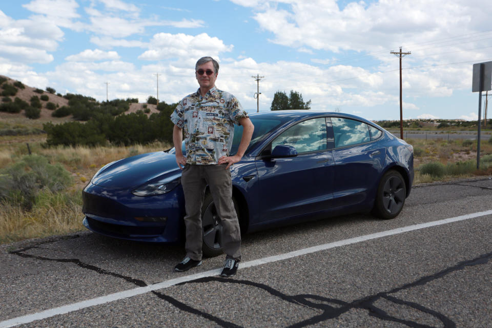 Howard Coe poses in front of his wife's Tesla sedan on Tuesday, Sept. 14, 2021, on a road near Nambé Pueblo outside of Santa Fe, N.M. Coe welcomed the opening of a new Tesla store and repair shop where he can pickup an SUV he's buying. Last year, he and his wife had to pick up her car in Denver, Colo., about five hours away, because of New Mexico laws that bar companies like Tesla from selling cars directly to customers. (AP Photo/Cedar Attanasio)