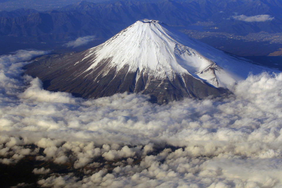 FILE - In this Dec. 8, 2010 file photo, snow-covered Mount Fuji, Japan's highest peak at 3,776-meters tall (12,385 feet), is seen from an airplane window. Those who want to climb one of the most popular trails of the iconic Japanese Mount Fuji will now have to reserve ahead and pay a fee as the picturesque stratovolcano struggles with overtourism, littering and those who attempt rushed “bullet climbing,” putting lives at risk. (AP Photo/Itsuo Inouye, File)