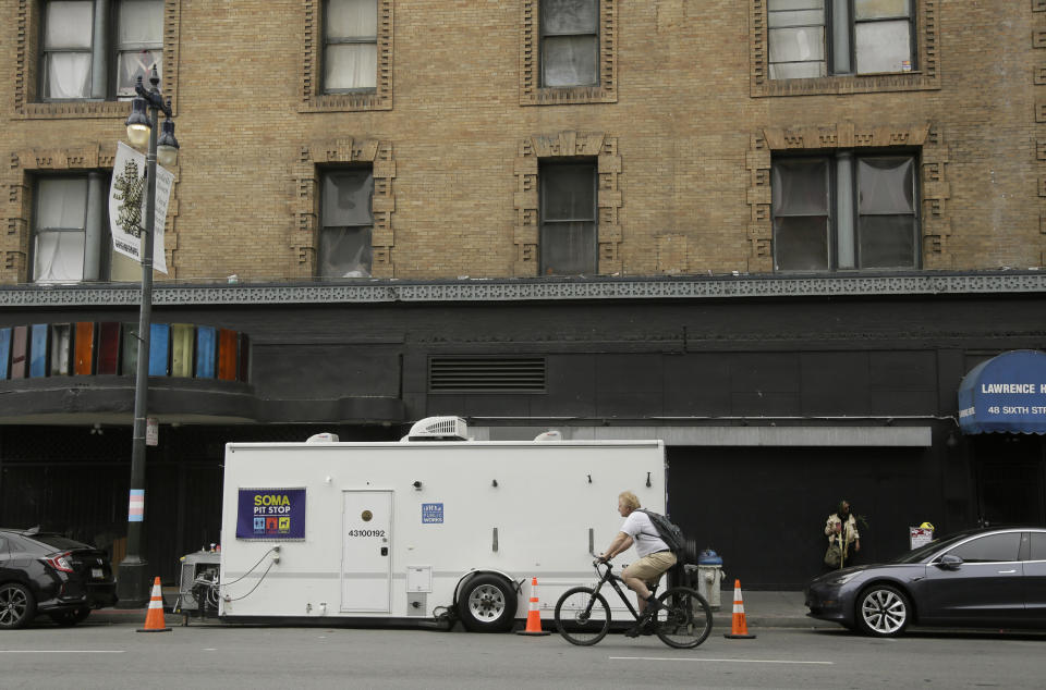 A man rides his bicycle past a "Pit Stop" public toilet on Sixth Street, Thursday, Aug. 1, 2019, in San Francisco. A 5-year-old portable toilet program in San Francisco that provides homeless people with a private place to go has expanded to 25 locations in the city and has spread to Los Angeles. Not everyone who uses the “Pit Stop” toilets is homeless, but advocates say steam cleaning requests have dropped in surrounding areas. (AP Photo/Eric Risberg)