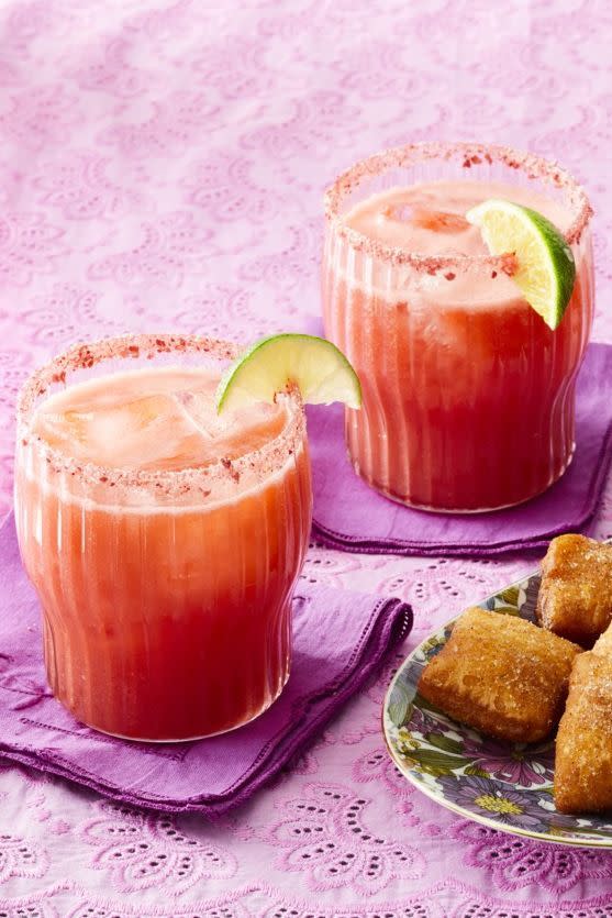 strawberry margaritas in two glasses with lime and plate with snacks