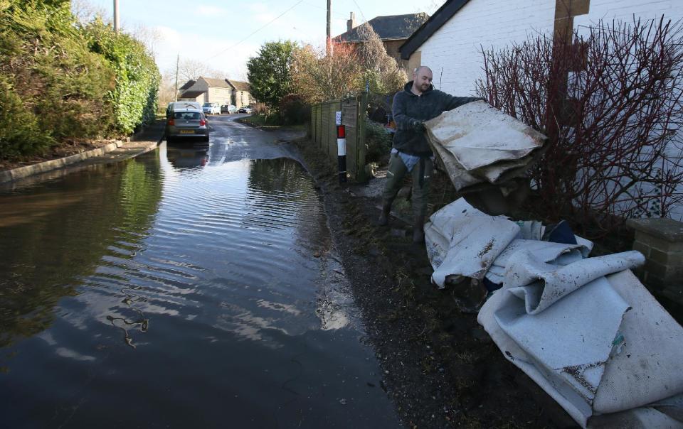 In this photo taken Sunday Feb. 2, 2014, Kris Davies gets rid of carpeting from his house after it was flooded on Jan. 2, he was forced to leave the house and returned Jan. 31 to begin the clear up in Thorney, Somerset, England. Here on the Somerset Levels _ a flat, marshy region of farmland dotted with villages and scored by rivers and ditches _ it's often wet. But not this wet. Thousands of acres of this corner of southwest England have been under water for weeks, some villages have been cut off for more than a month, and local people forced to take boats to get to school, work and shops are frustrated and angry. Some blame government budget cuts and environmental bureaucracy. Others point to climate change. Even plump, endangered water voles are the target of ire.(AP Photo/Alastair Grant)