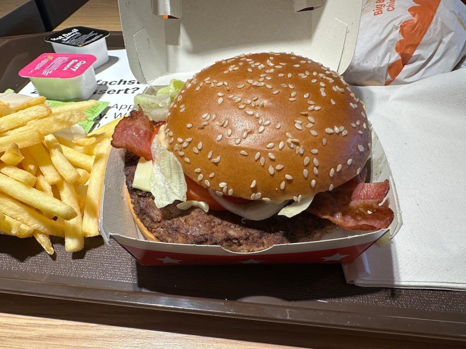 mcdonalds burger shiny sesame bun on top of lettuce bacon and burger patty in white box next to french fries