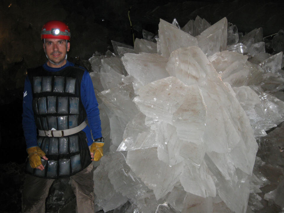 Wearing an ice-pack vest, Mario Corsalini stands by a giant rosette of gypsum in the Naica Mine's crystal cavern. <cite>Mike Spilde/University of New Mexico</cite>