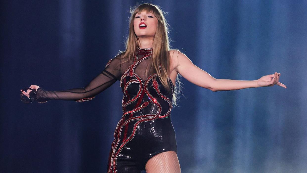  Taylor Swift in her Reputation outfit standing with her arms out . 