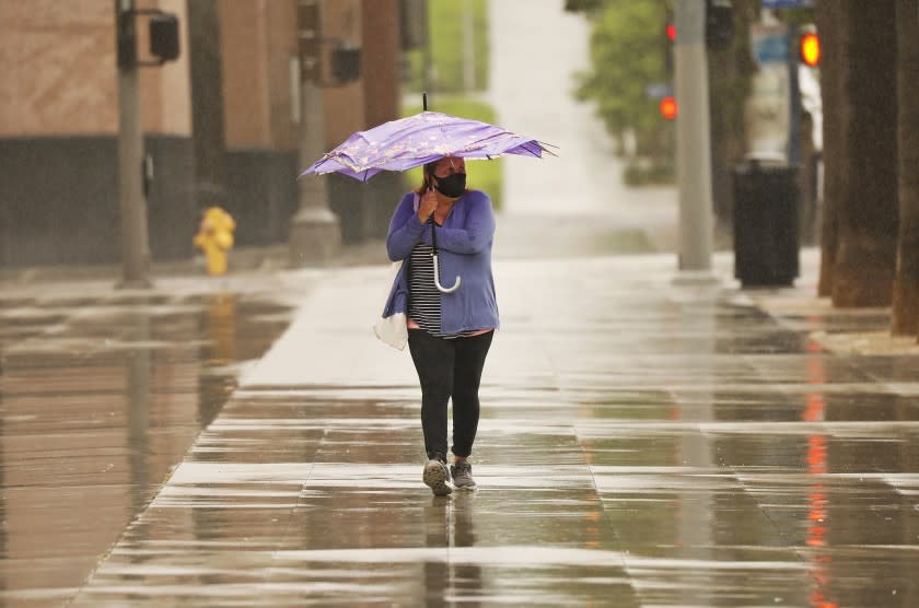 LOS ANGELES, CA - MAY 18: Blanca Torres wears her face mask and umbrella in downtown Los Angeles Monday morning as rain douses the southland today amid a cooling trend. National Weather Service meteorologist Kristen Stewart said the rain and falling temperatures are the product of a cold front spawned by a low-pressure system off Northern California and temps are expected to be several degrees lower than last week's. Downtown on Monday, May 18, 2020 in Los Angeles, CA. (Al Seib / Los Angeles Times)