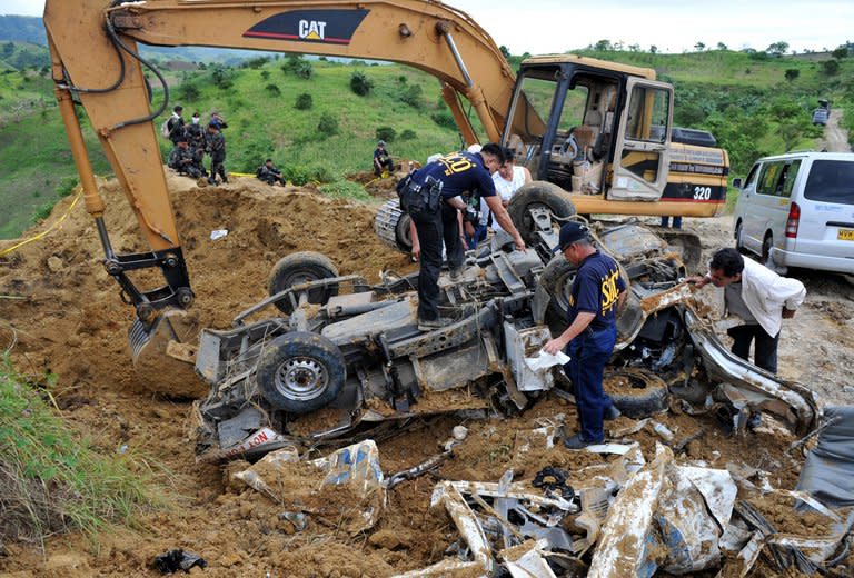 This file photo, taken on November 25, 2009, shows police investigators looking for evidence next to a backhoe, on a mangled vehicle unearthed at the crime scene where human remains were dug up from a shallow grave as investigators try to find more bodies, victims of a massacre after gunmen shot people in the town of Ampatuan, Maguindanao province in the southern Philippines