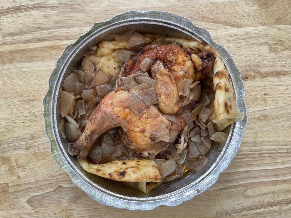 Pieces of chicken in a bowl resting on pieces of flatbread and stewed onions.