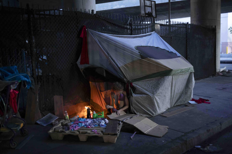 A homeless woman ignites a fire using cardboard beneath the section of Interstate 10 that has been closed due to a recent fire in Los Angeles, Tuesday, Nov. 14, 2023. At least 16 homeless people, including a pregnant woman, were evacuated when flames ripped through storage yards beneath the Los Angeles freeway. The disaster has renewed attention on the city's inability to protect the thousands of unhoused residents living in such perilous locations across the city. (AP Photo/Jae C. Hong)