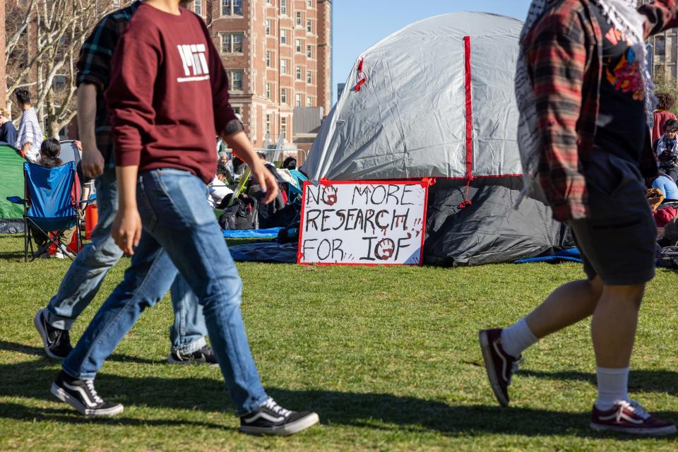 Protest sign reading "No More Research for IGF" in front of a tent with people passing by