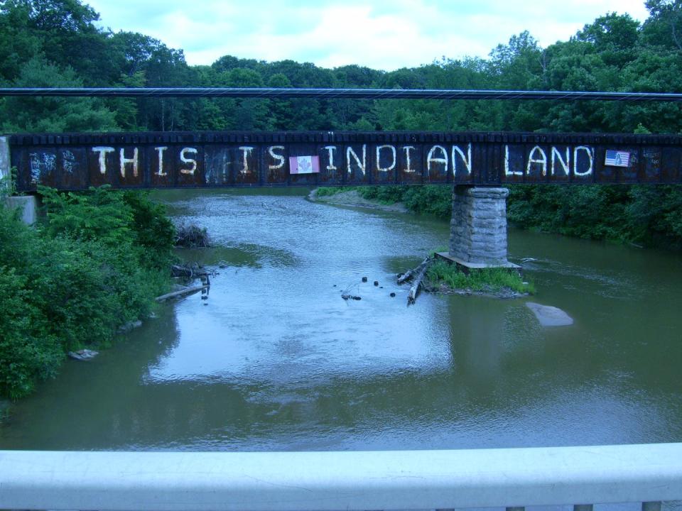 A bridge with the graffiti, 'This is Indian Land' over a river.