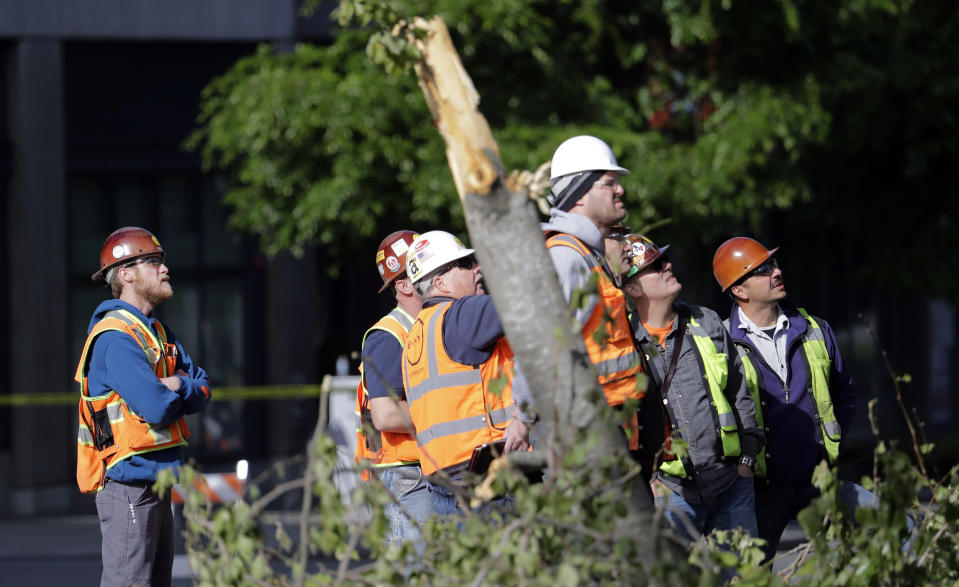 Workers look on where debris is being cleared from where a crane atop a building under construction collapsed a day earlier, Sunday, April 28, 2019, in Seattle. The construction crane fell from a building on Google's new campus during a storm that brought wind gusts, crashing down onto one of the city's busiest streets and killing multiple people. (AP Photo/Elaine Thompson)