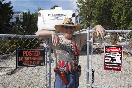 Wearing two revolvers, Doug Varrieur poses at a gate to his home in Big Pine Key in the Florida Keys March 5, 2014. REUTERS/Andrew Innerarity