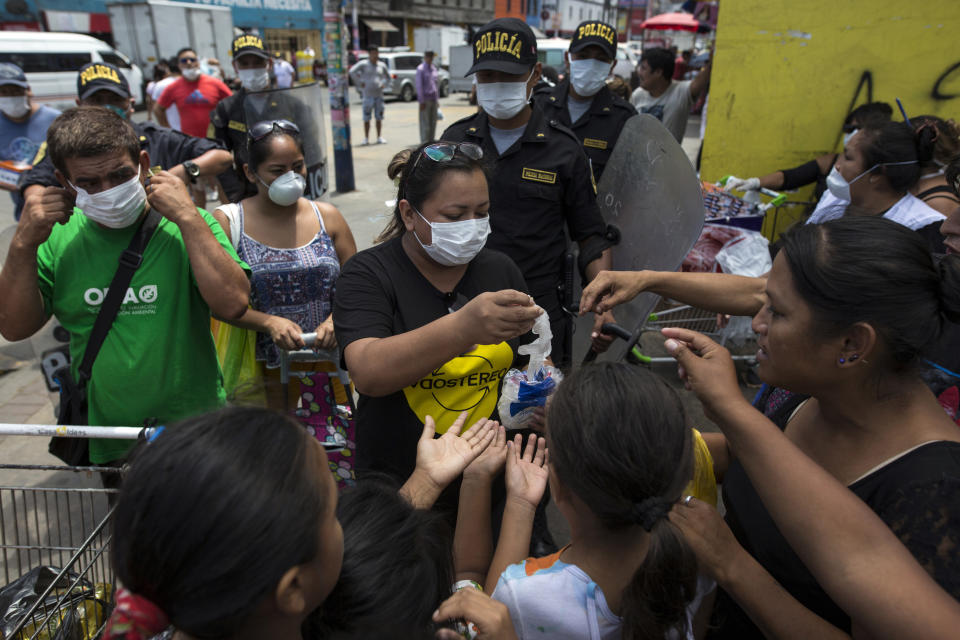 In this March 19, 2020 photo, Cesar Alegre, far left, and fellow residents who share a sprawling rundown house, receive free protective gear to help curb the spread of the new coronavirus, outside a popular food market in Lima, Peru. Alegre and his children, accompanied by a handful of residents, start out by walking about 2 miles (3 kilometers) to the market where merchants give them potatoes, meat bones and overripe fruit that nobody wants to buy. (AP Photo/Rodrigo Abd)