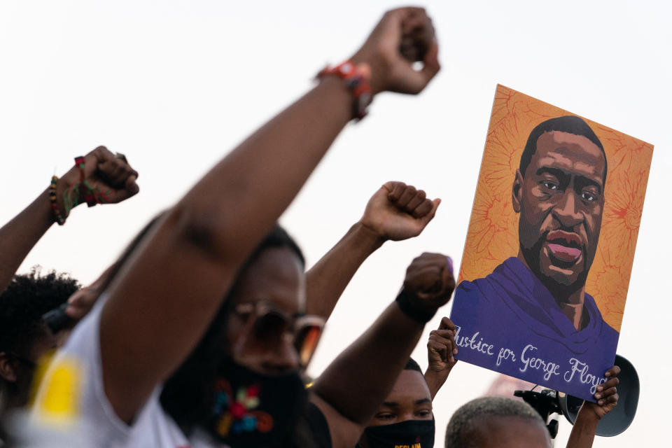 African Americans at a rally raise their fists and hold an orange and purple poster of George Floyd saying: Justice for George Floyd.