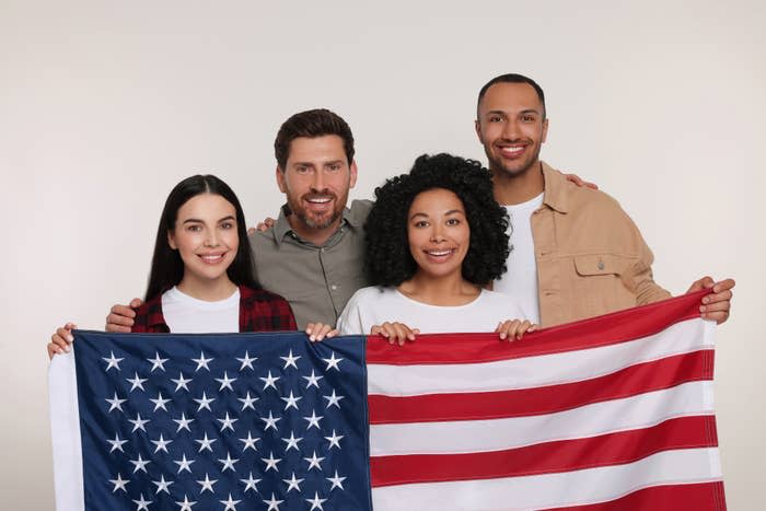 Four smiling friends holding an American flag together, expressing unity and patriotism