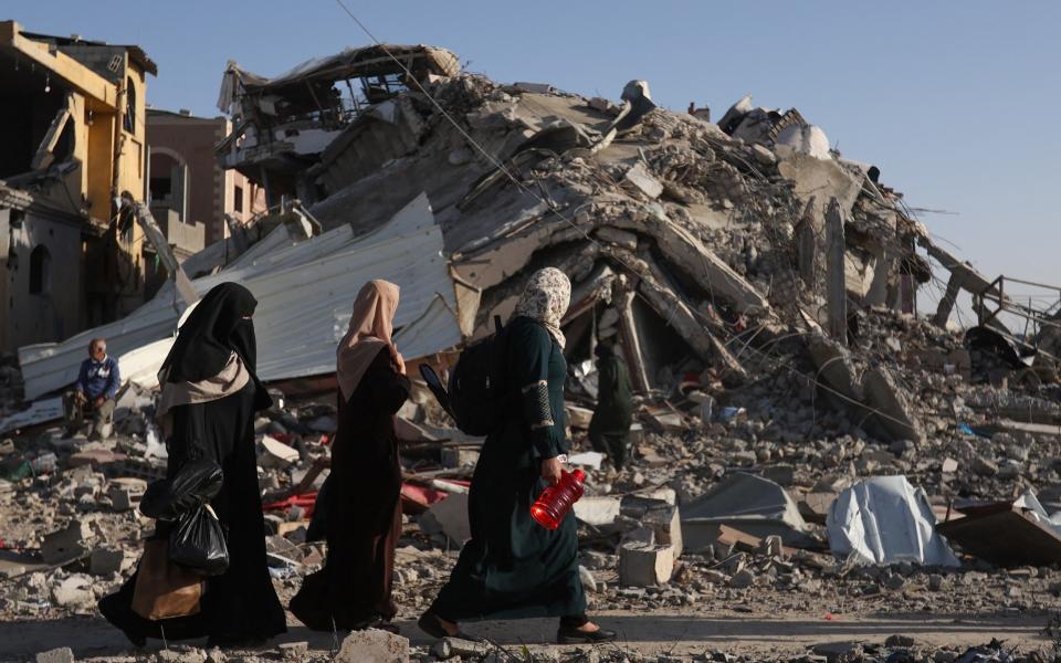 Displaced Palestinians return to their homes as they walk near houses destroyed in an Israeli strike