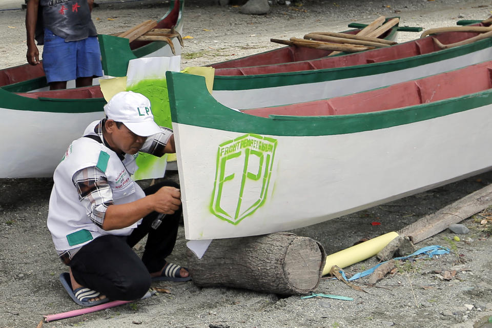 In this April 2, 2019, photo, a member of Islamic Defenders Front paints their group's logo as they help local fishermen to build boats at a fishing village affected by the 2018 tsunami in Palu, Central Sulawesi, Indonesia. The Islamic Defenders Front, known for vigilante actions against gays, Christmas decorations and prostitution, has over the past 15 years repurposed its militia into a force that's as adept at searching for earthquake victims as it is at inspiring fear. (AP Photo/Tatan Syuflana)