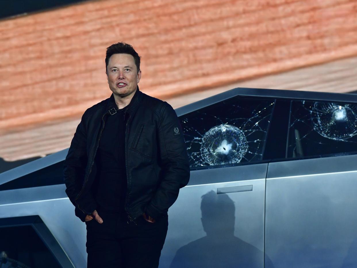 Elon Musk standing in front of a Cybertruck with shattered windows.