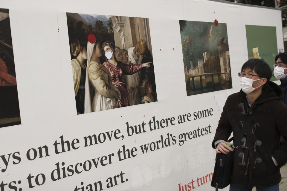 Tourists wearing protective masks look at a poster promoting art that has been modified by adding a face mask to a woman's face, in Venice, Saturday, Feb. 29, 2020. A U.S. government advisory urging Americans to reconsider travel to Italy due to the spread of a new virus is the "final blow" to the nation's tourism industry, the head of Italy's hotel federation said Saturday. Venice, which was nearing recovery in the Carnival season following a tourist lull after record flooding in November, saw bookings drop immediately after regional officials canceled the final two days of celebrations this week, unprecedented in modern times. (AP Photo/Francisco Seco)