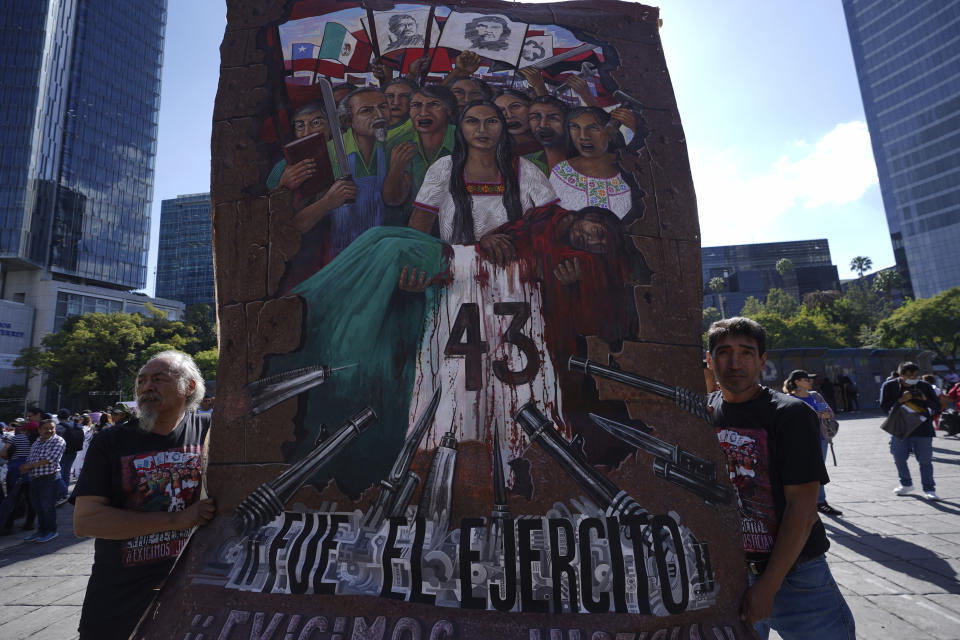 Dos hombres llevan una pancarta sobre los 43 estudiantes de Ayotzinapa mientras familiares y simpatizantes marchan por el noveno aniversario de su desaparición, en Ciudad de México, el martes 26 de septiembre de 2023. (AP Foto/Marco Ugarte)