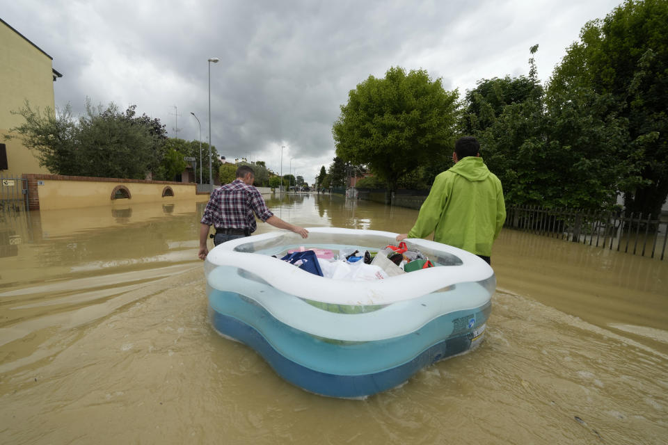 People use a plastic portable pool to carrie bags and personal effects in a flooded road of Lugo, Italy, Thursday, May 18, 2023. Exceptional rains Wednesday in a drought-struck region of northern Italy swelled rivers over their banks, killing at least eight people, forcing the evacuation of thousands and prompting officials to warn that Italy needs a national plan to combat climate change-induced flooding. (AP Photo/Luca Bruno)