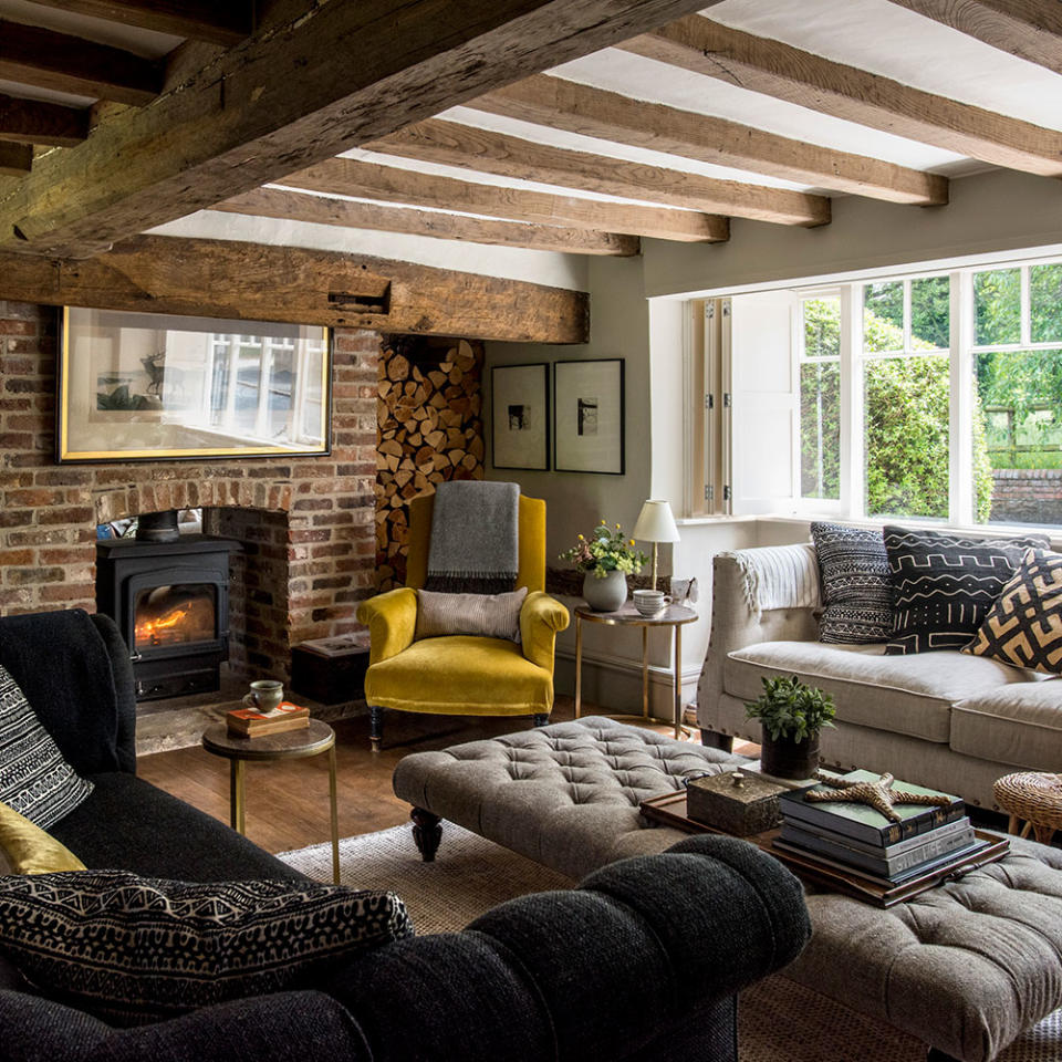 <p> This charmingly rustic living room has all the ingredients for a traditional cottage feel. The inglenook fireplace and exposed beams set a rustic tone, while modern design touches such as the squashy sofas, metallic side tables and a bold mustard velvet armchair bring the look up to date. </p> <p> The dark furnishings and soft textures in this living room create an intimate space, ideal for entertaining on cosy nights in. </p>