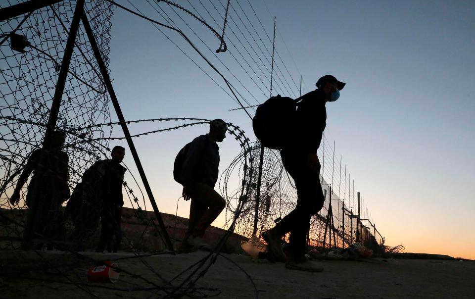 Palestinian workers cross illegally into Israeli areas through a hole in Israel's barrier fence near the Mitar checkpoint and the village of al-Dahriya, south of Hebron in the occupied West Bank, early on Aug. 17, 2020.