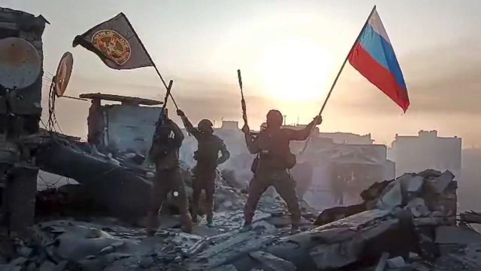 Wagner Group military company members wave Russian and Wagner flags atop a damaged building in Bakhmut, Ukraine, n this screen grab taken from video released by Prigozhin Press Service May 20. (Prigozhin Press Service via AP)