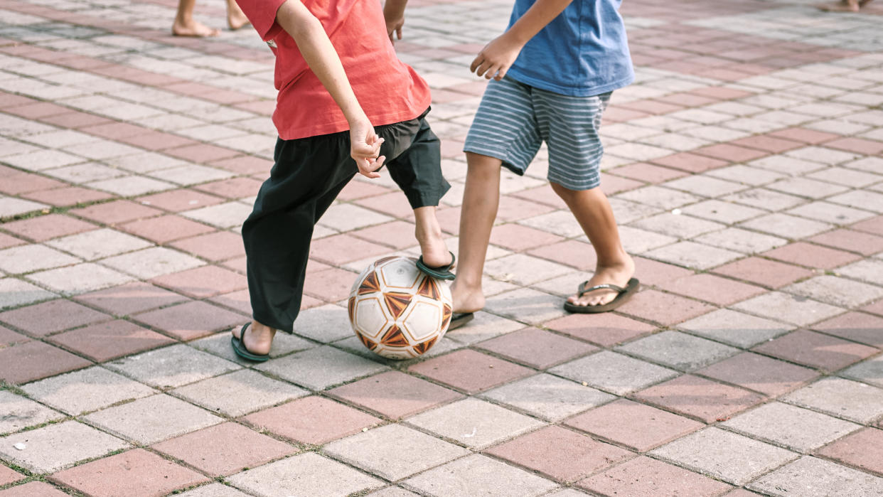 children's leg playing football with sandals on a paving stone