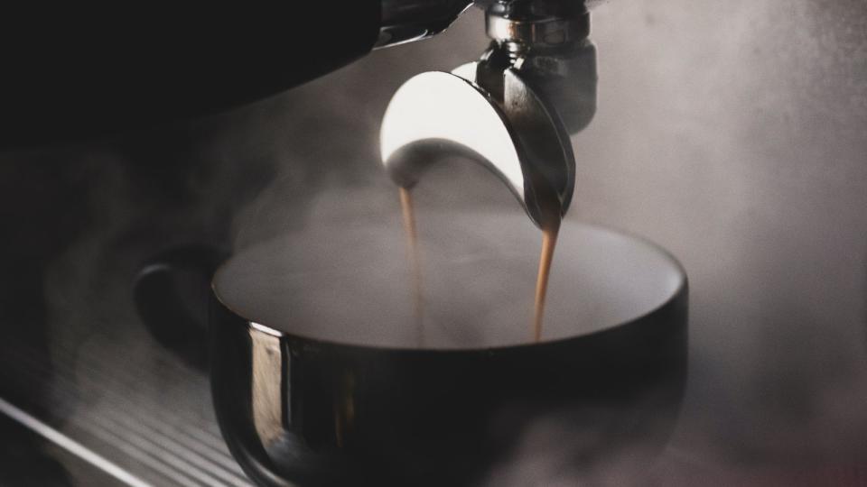 An espresso machine pouring a steaming shot into a black coffee mug