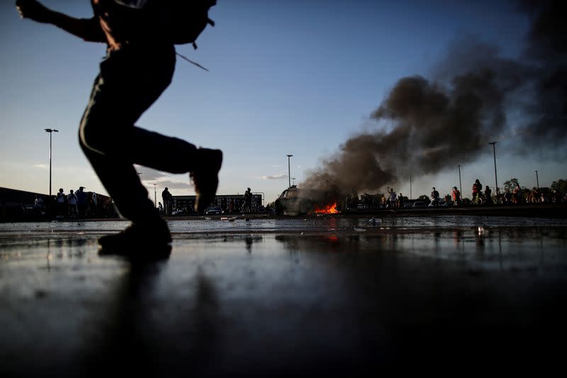 Un hombre pasa junto a un coche en llamas en el aparcamiento de una tienda Target durante las protestas en Minneapolis, Minnesota, EEUU