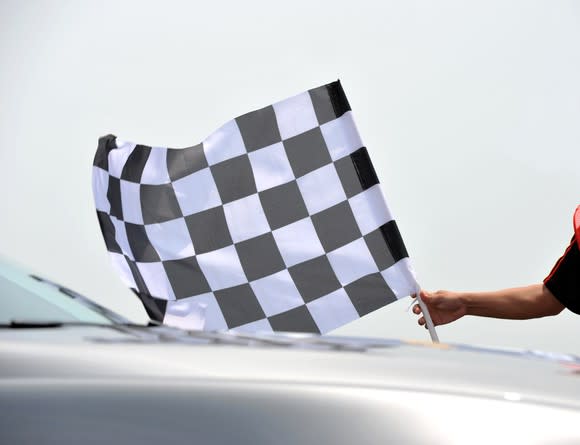 A person holding a checkered flag near a car.