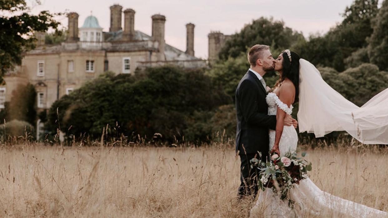 Bride and groom kissing in a field outside a wedding venue