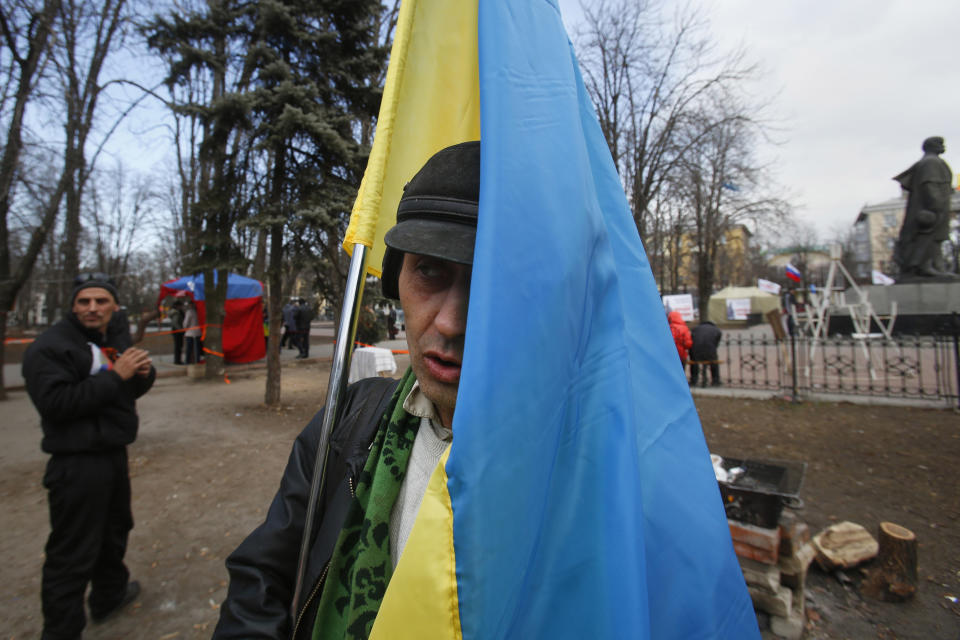 In this photo taken Tuesday, March 11, 2014, pro Russian activists, one of them holding a Ukrainian flag, stand around a camp they set up in Luhansk, eastern Ukraine. In Ukraine’s coal-fired industrial east, a potent mix of economic depression, ethnic solidarity and nostalgia for the certainties of the Soviet past among those old enough to remember them have many people demanding the right to become part of Russia as well. (AP Photo/Sergei Grits)