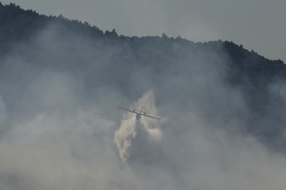 An aircraft drops water on a fire during a wildfire near Tatoi, in northern Athens, Greece, Saturday, Aug. 7, 2021. Wildfires rampaged through massive swathes of Greece's last remaining forests for yet another day Saturday, encroaching on inhabited areas and burning scores of homes, businesses and farmland. (AP Photo/Petros Karadjias)
