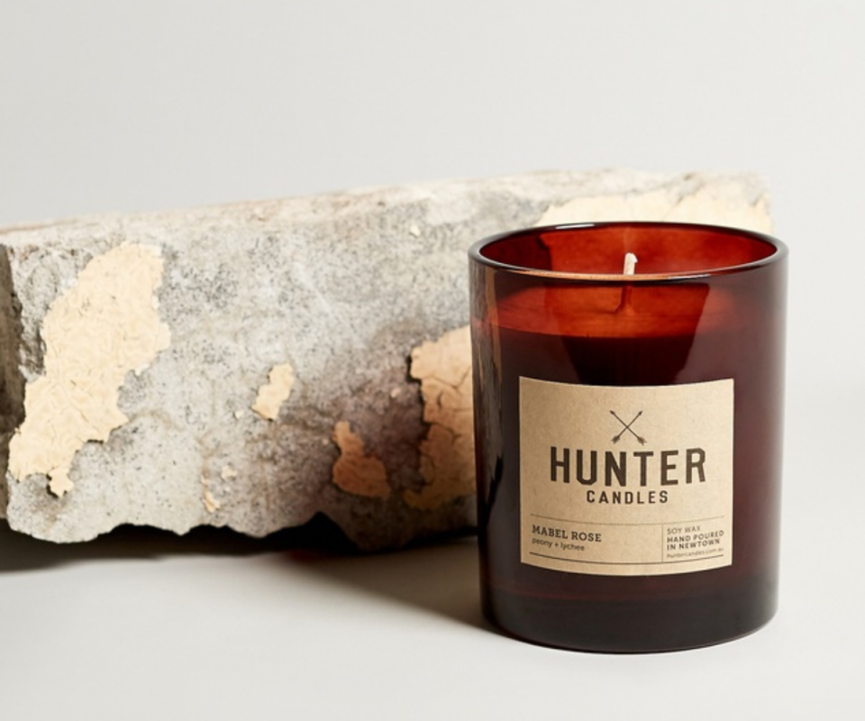 A bronze glass candle on a white background with a chipped grey brick behind it.