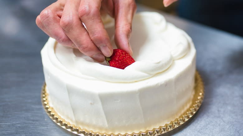 A hand placing a strawberry on a cake
