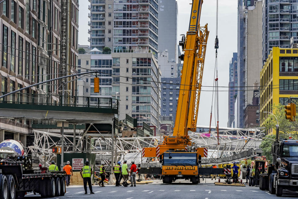 Work crews standby as a crane lifts the extension arm from a hi-rise construction crane, which broke away yesterday and plummeted to the street after the crane caught fire, Thursday July 27, 2023, in New York. (AP Photo/Bebeto Matthews)