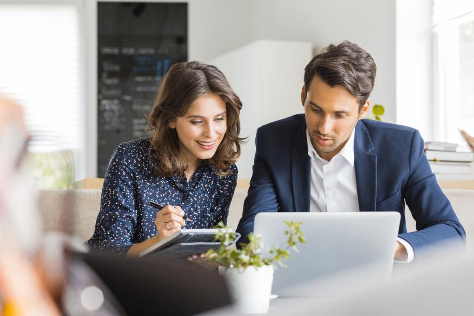 Two people in an office study something on a laptop.