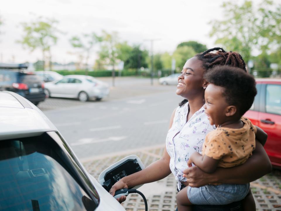 Mother holding her son while charging her electric vehicle