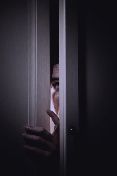 A person's eyes and one hand visible through a slightly opened door