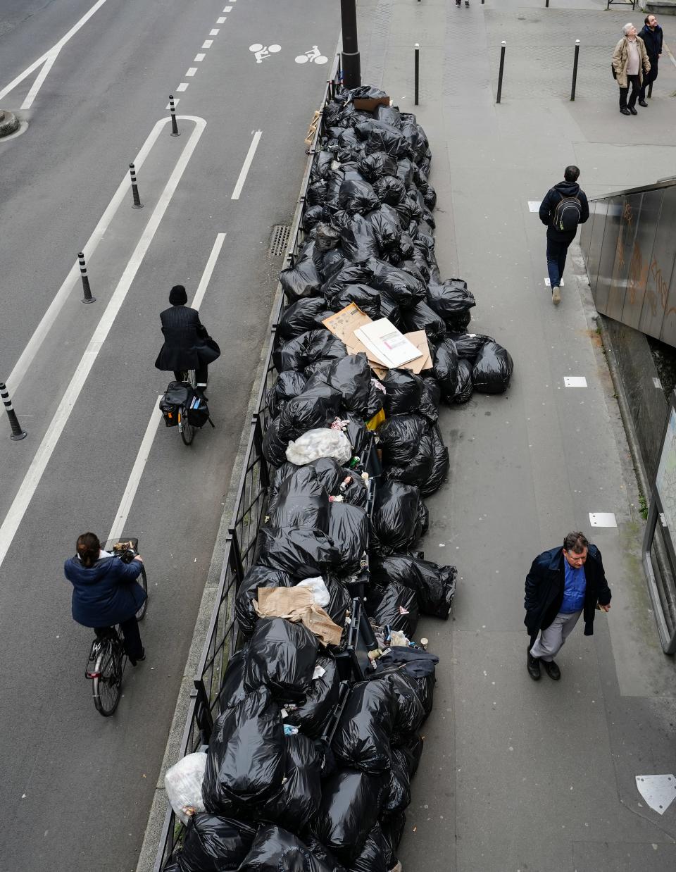 People walk and ride past uncollected garbage in Paris, Friday March 17, 2023, as sanitation workers are on strike.
