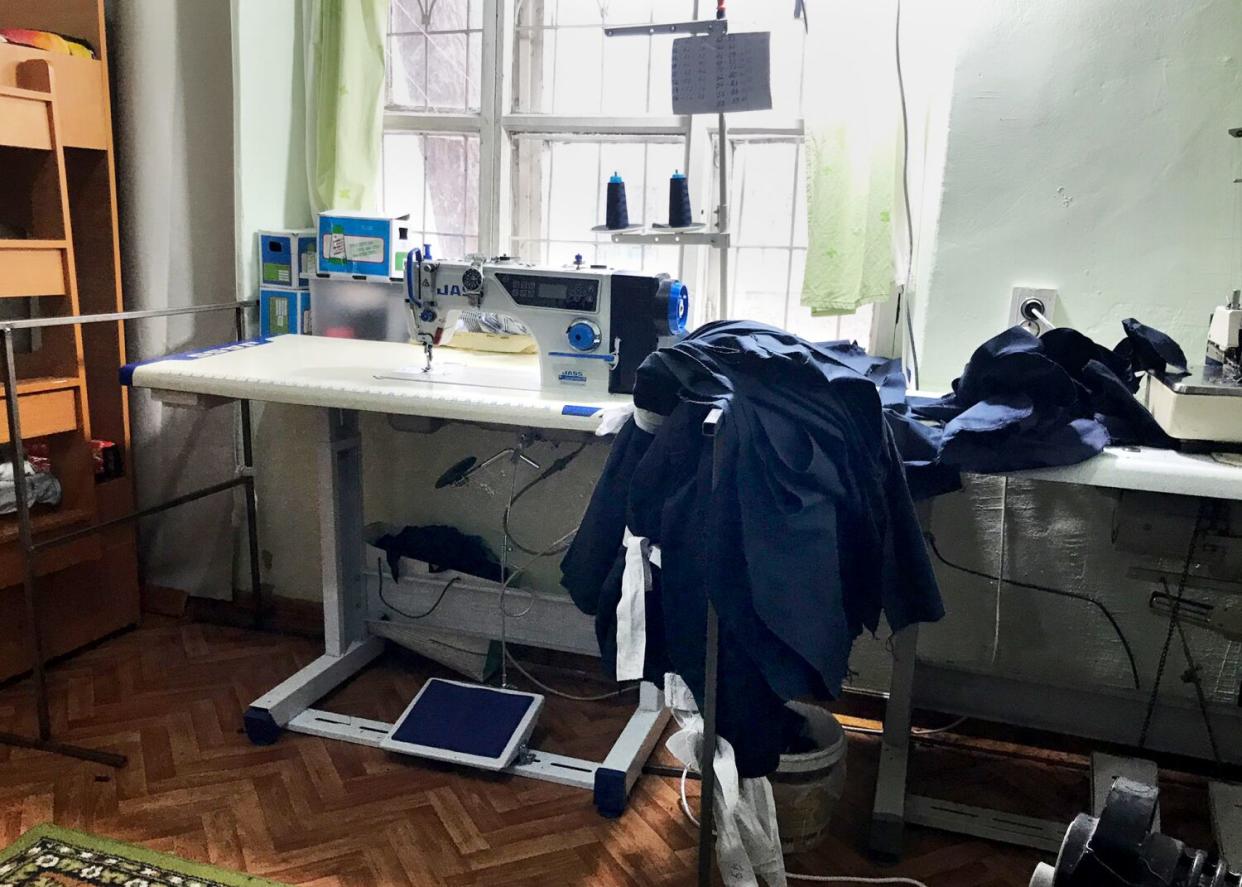 A still life of a sewing machine set up near a window. A pile of dark cloth is draped over.