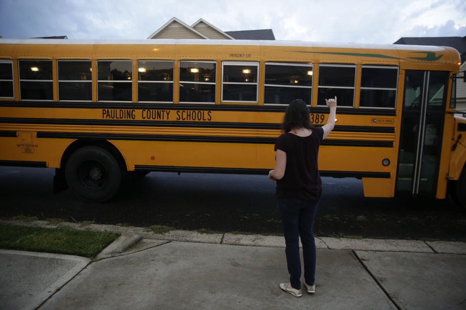 Rachel Adamus waves goodbye to her two children, Paul and Neva, as they ride the bus for the first day of school on Monday, Aug. 3, 2020, in Dallas, Ga. (AP Photo/Brynn Anderson)