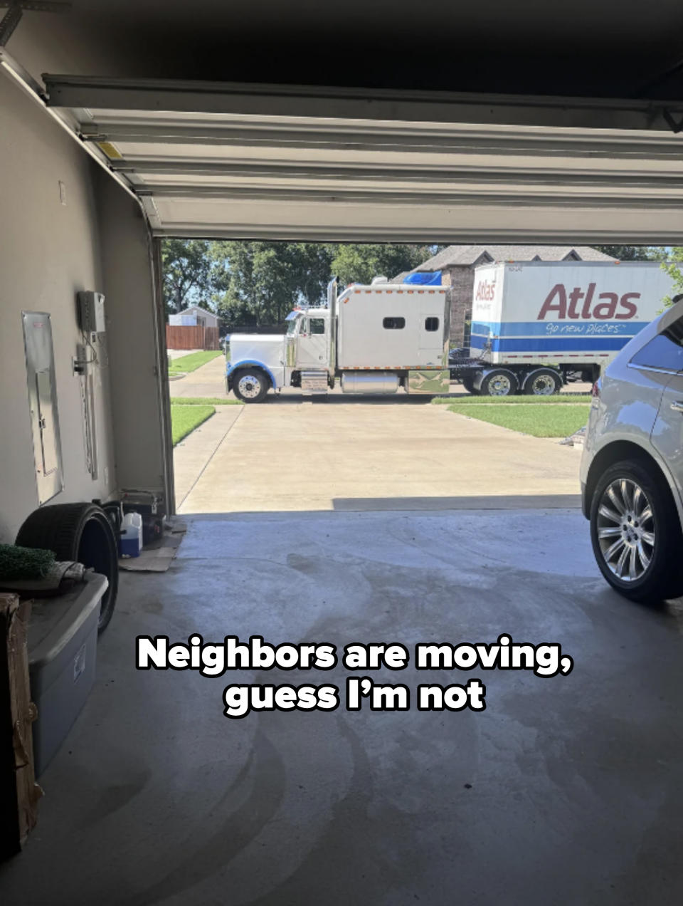 View from inside a garage looking out to a driveway where a moving truck labeled "Atlas" is parked