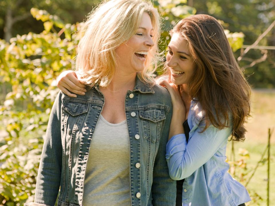 Mother and daughter laugh as they walk together through backyard garden in rural coastal home in Maine