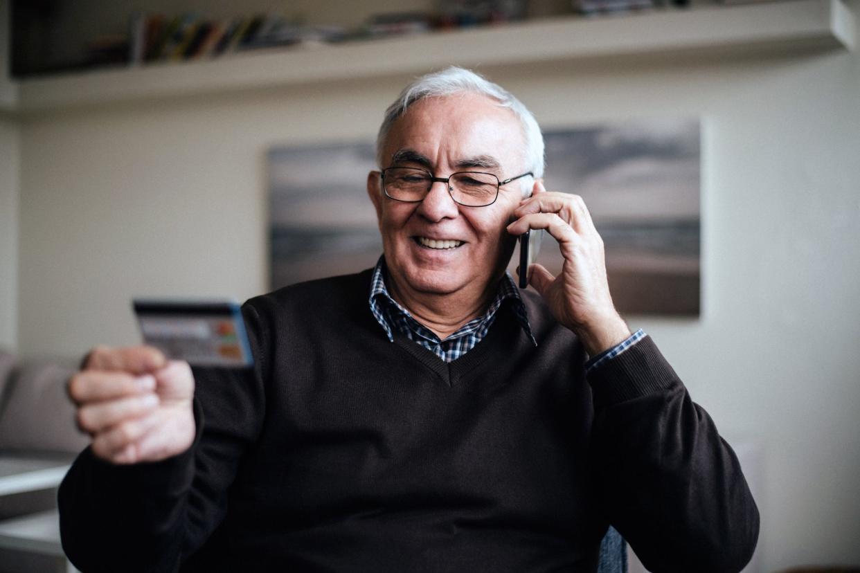 senior man talking on phone smiling holding credit card