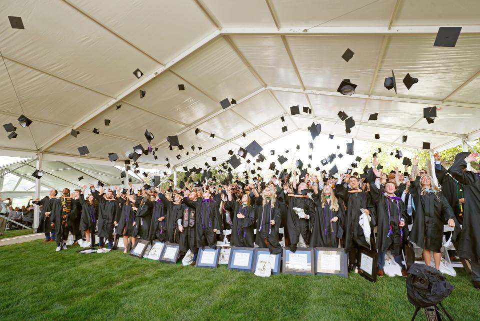Adrian College graduates throw their caps at the end of the 2023 spring commencement ceremony. A large, temporary pavilion was erected on the college Mall to cover the students due to the chance of inclement weather.